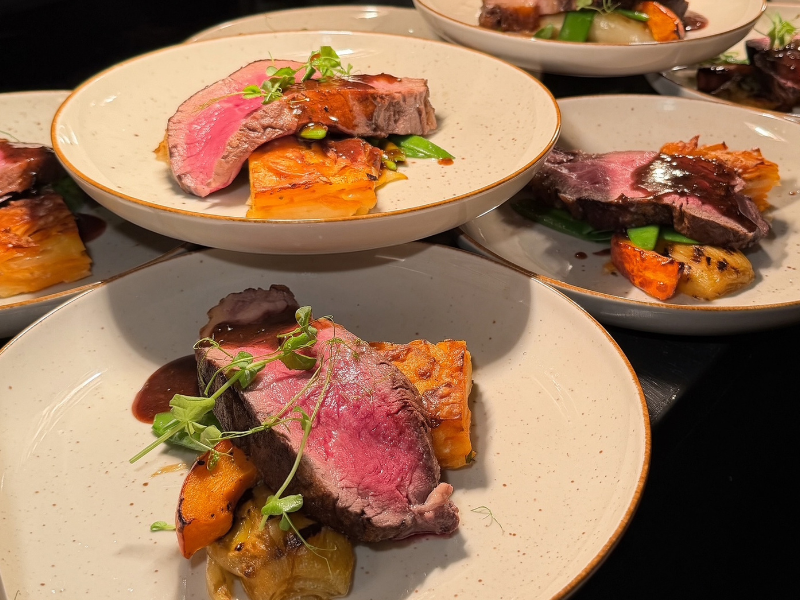 Meerdere borden met rosé gebakken vlees, groenten en saus, klaar om geserveerd te worden.